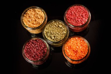 siyah ayna arka plan üzerinde pembe, sarı, turuncu, yeşil ve kırmızı renkli deniz tuzu ile dolu küçük cam kavanozlara Üstten Görünüm