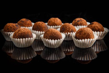 sağlıklı yararlı organik el yapımı yuvarlak çikolata şekerleme büyük grup siyah ayna arka plan üzerinde kahverengi kakao tozu ile dekore edilmiş