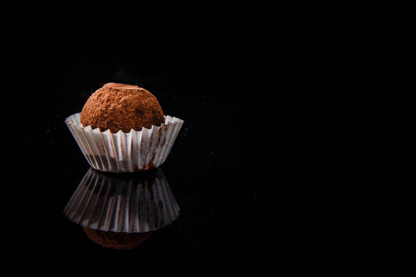 Крупный план полезных органических круглых шоколадных конфет ручной работы, украшенных коричневым какао порошком на черном фоне зеркала
