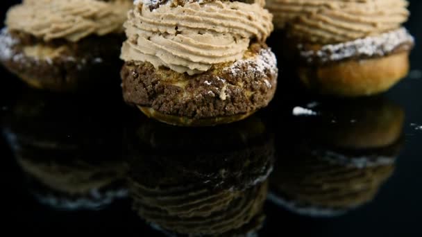 特写镜头全景从反映上的一套法国甜点 Choux 糕点充满焦糖霜在黑色镜子背景上 — 图库视频影像