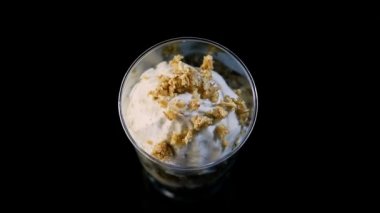 siyah arka plan üzerine küçük yuvarlak plastik bardaklarda servis granola ile dekore edilmiş iki muzlu mousse tatlı insan el koymak