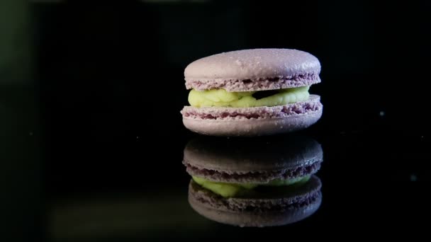 特写镜头紫罗兰色法国甜点马卡龙与绿色奶油填充服务在黑色镜子背景与反射 — 图库视频影像