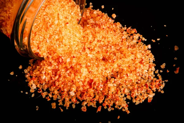 Крупный план большая оранжевая органическая морская соль выливается из маленькой стеклянной банки — стоковое фото