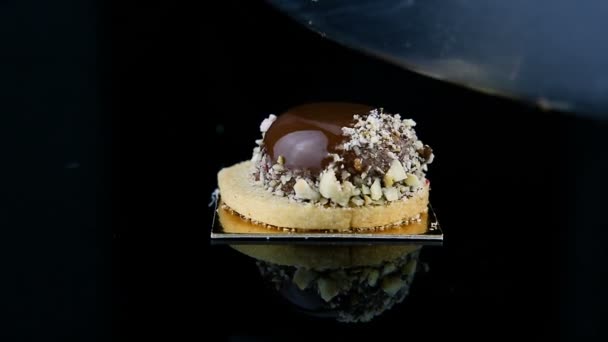ムース菓子デザート チョコレート艶出しで覆われ 砕いたナッツ ブラック ミラーの背景にナイフで半分にカットで飾られたフランスのシングル — ストック動画