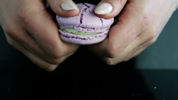 特写镜头人的手打破在半紫罗兰色法国甜点马卡龙与绿色奶油填充在黑色的镜子背景 — 图库视频影像