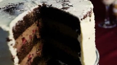 closeup büyük çikolatalı kek karamel ile dilimlenmiş ve yavaş yavaş beyaz krema ile dekore edilmiş doldurma kiraz etrafında döner