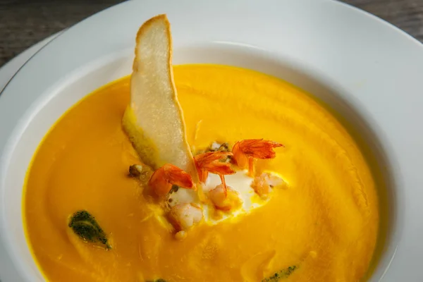 Closeup yellow cream soup decorated with prawns tails and dried bread — Stock Photo, Image