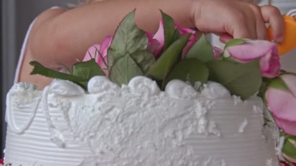 クローズアップ小さなブロンドの女の子はバラで飾られた白いクリーミーなウェディングケーキの小片を試してみてください — ストック動画