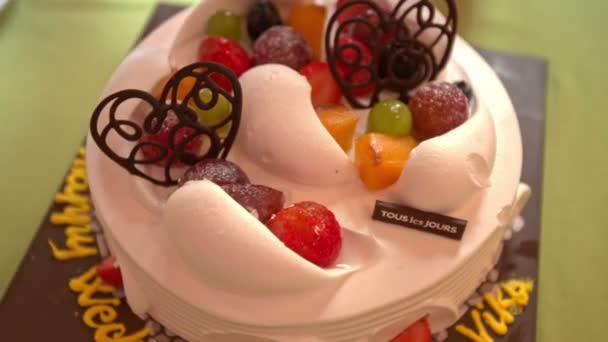 チョコレートハートのシンボルと緑のテーブルに提供されるトロピカルフルーツの装飾とクローズアップ大きな白いクリームのウェディングケーキ — ストック動画