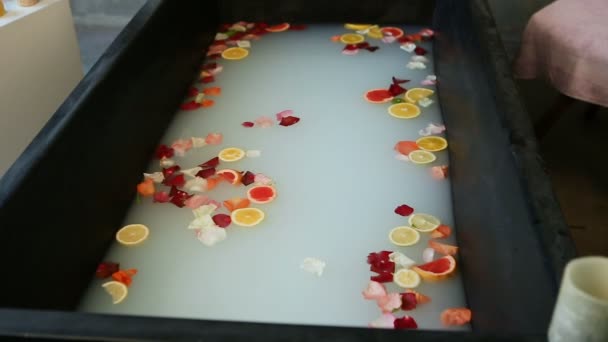 Zoom in at hot cosmetic bath with milk, citrus slices, and rose petals — Stock Video