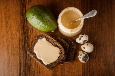 kavanozda tahin yağı üst görünümü, çavdar ekmeği, avokado, ve bıldırcın yumurtası