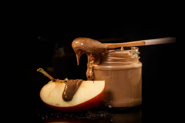 Closeup chocolate peanut butter in glass jar with slice of apple — Stock Photo, Image