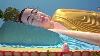 Vietnam 'daki Budist tapınak parkında filizlenen ağaçların arasında tepeden tırnağa uzanan altın sarısı Buda' yı kapatın.