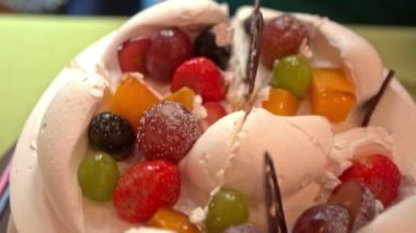 Üst manzara. Masanın üzerinde çikolata kalp sembolü ve tropikal meyve süslemesi olan büyük, beyaz bir düğün pastası.