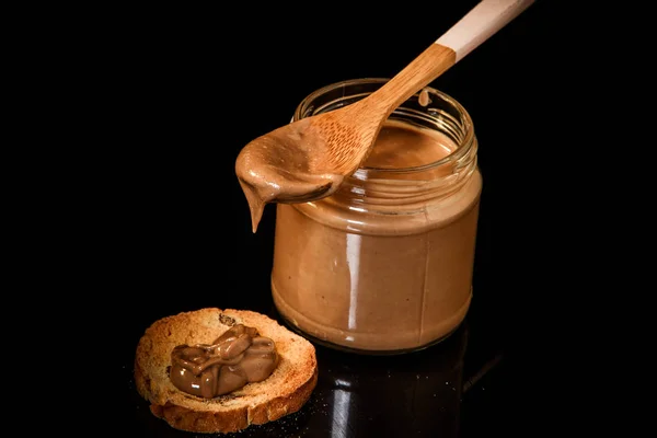 Manteiga de amendoim de chocolate closeup em frasco de vidro e pequeno biscoito — Fotografia de Stock