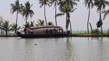 Alappuzha, Kerala / Hindistan - 12 Şubat 2012: Mavi gökyüzü ufkuna karşı geniş nehir panoraması ve Hindistan 'da palmiye kıyısında 12 Şubat' ta Alappuzha 'da büyük kahverengi ahşap yüzen ev bozkırları