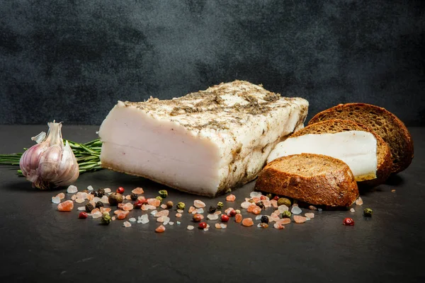 Sliced salted lard in black pepper with spices, garlic, bread and cucumbers — Stock Image Sliced salted lard in black pepper with spices, garlic, bread and cucumbers Stock Photo