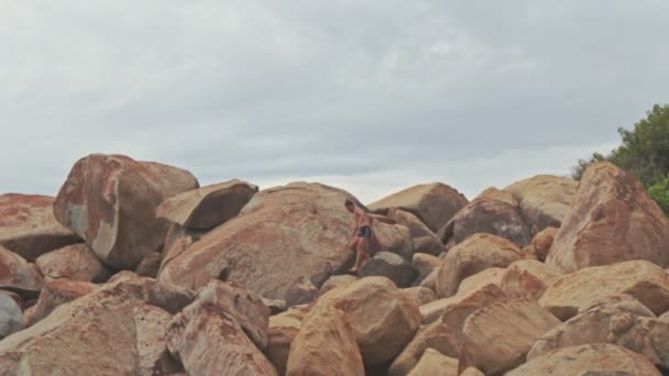 Guy salta sobre un gran montón de rocas en la playa de Hill Foot — Vídeo de stock