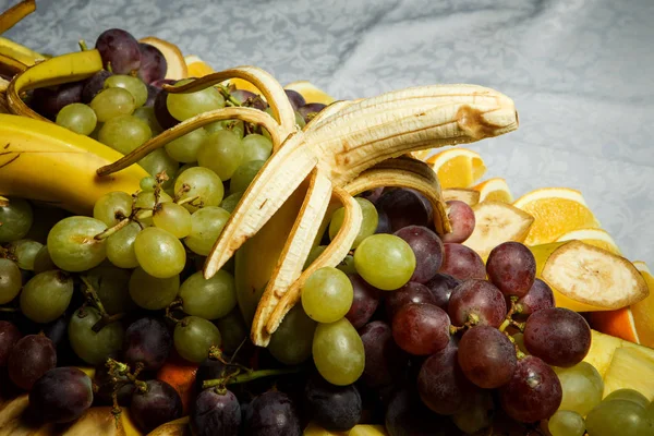 Uvas inteiras sortidas e frutas tropicais fatiadas no prato grande — Fotografia de Stock