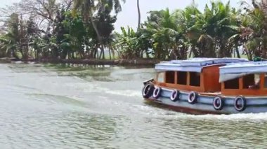 Alappuzha, Kerala / Hindistan - 12 Şubat 2012: Yakından bakıldığında turist teknesi Hindistan 'da 12 Şubat' ta Alappuzha 'da büyük palmiyelere karşı geniş nehir boyunca hızla ilerliyor