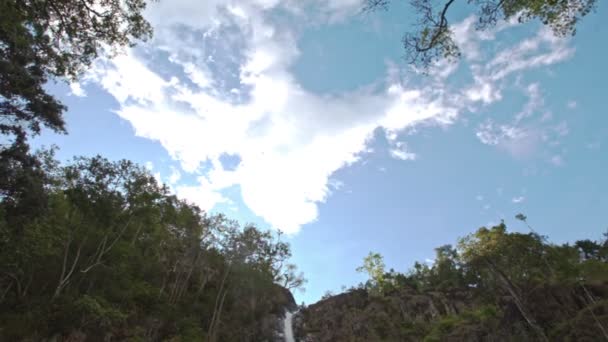 白い雲と青い空からのパノラマビュー熱帯国立公園の岩や緑の植物の間の高い滝 — ストック動画