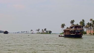 Alappuzha, Kerala / Hindistan - 12 Şubat 2012: Palmiye kıyılarına karşı geniş nehir panoraması ve Hindistan 'da 12 Şubat' ta Alappuzha 'da büyük kahverengi ahşap yüzer ev kameraya yaklaşıyor