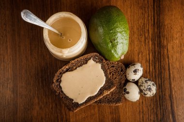kavanozda tahin üst görünümü, çavdar ekmeği, avokado, üç bıldırcın yumurtası