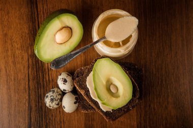 tahin, çavdar ekmeği, dilimlenmiş avokado ve küçük yumurta üst görünümü