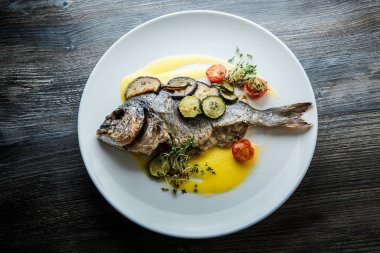 dilimlenmiş sebzelerle servis edilen lezzetli balıkların üst görünümü