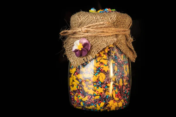 Closeup glass jar with different shaped colorful topping — Stock Photo, Image