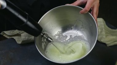 Kapalı kadın elleri derin metal kâse içinde çırparak yumurta beyazı çırpıyor.