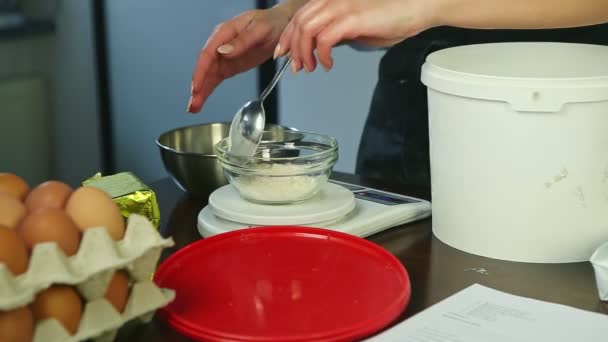 Zbliżenie kobieta wkłada mąkę po łyżce do małej miski stojącej na wagi elektronicznej — Wideo stockowe