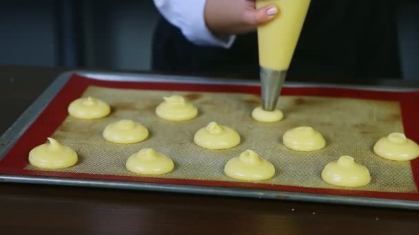 Close-up vrouwelijke handen vormen custard koekjes choux door gebak zak op bakpallet — Stockvideo