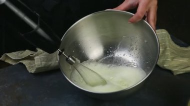 Yakın plan aşçıbaşı elleri derin metal kasede çırparak yumurta beyazı çırpıyor.