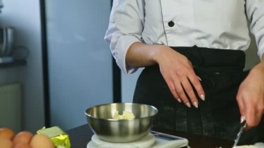 Yakın plan kadın elleri bıçakla kesilmiş taze tereyağı elektronik teraziyle metal kaseye konmuş.