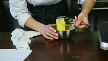 Yakın plan aşçı elleri çırparak çiğ yumurta sarılarını metal kasede şekerle karıştırıyor.