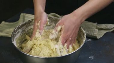 Kapalı kadın elleri büyük metal kasede yumuşak maya hamurunu çabucak yoğurur.
