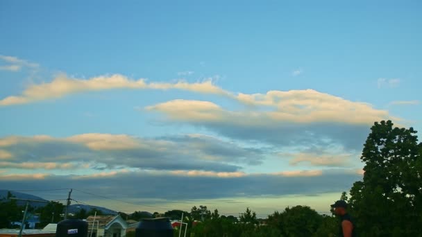 Stora fluffiga vita moln flyter på blå himmel ovanför små tropiska stadshus tak — Stockvideo
