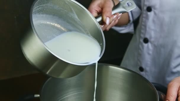 Slow motion closeup persoon begint te gekookte melk van steelpan gieten in metalen kom — Stockvideo