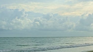 Büyük kabarık bulutların üzerindeki yavaş panorama beyaz dalgalarla mavi okyanusun üzerinde yüzer.