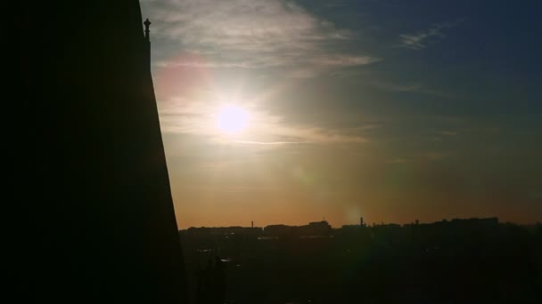 Nuvens brancas fluem lentamente acima do sol brilhante e da silhueta da cidade velha no por do sol — Vídeo de Stock