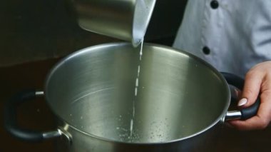 Ağır çekimde kadın tencereden metal kaseye kaynamış süt döker.