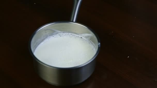 Soft focus closeup on milk boiling in small metal saucepan on black electric stove — Stock Video