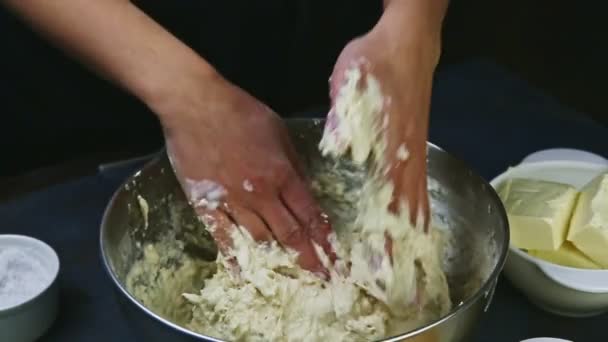 Кондитер крупным планом руками разминает мягкое дрожжевое тесто в большой металлической миске — стоковое видео