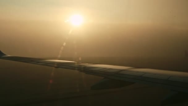 Vue rapprochée sur l'aile de l'avion depuis la fenêtre contre le soleil brillant à travers le brouillard au lever du soleil — Video