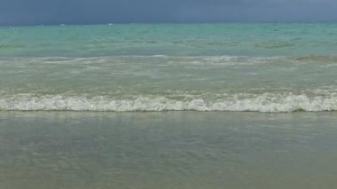 Mavi okyanusun küçük beyaz dalgaları kumlu sahilde karanlık fırtınalı gökyüzüne doğru yavaşça akıyor.