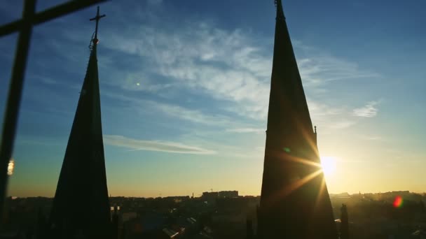 Gyllene sol gömmer sig bakom mörka silhuetter av höga kyrka spiror mot blå himmel — Stockvideo