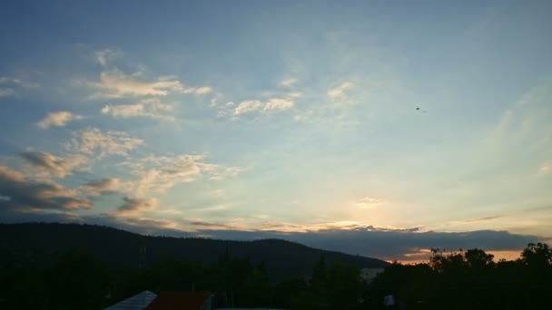 Kleiner schwarzer Drachen schwebt hoch am hell bewölkten Sonnenuntergangshimmel über schwarzen Mittelgebirgen — Stockvideo