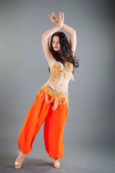 美しいです若いですスリムブルネット女の子でオレンジ腹ダンサー衣装リフト手アップダンスに対してグレー背景でスタジオ — ストック写真