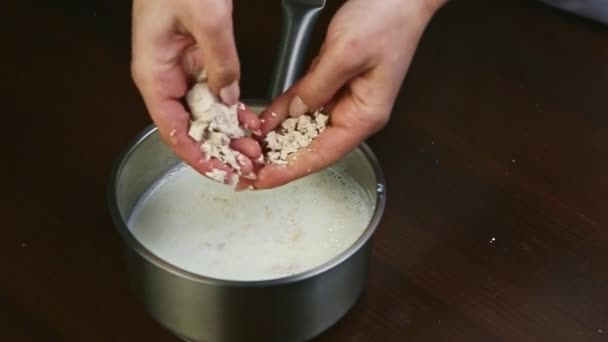 Slow motion closeup female hands crush dry yeast into hot milk in metal saucepan — Stock Video